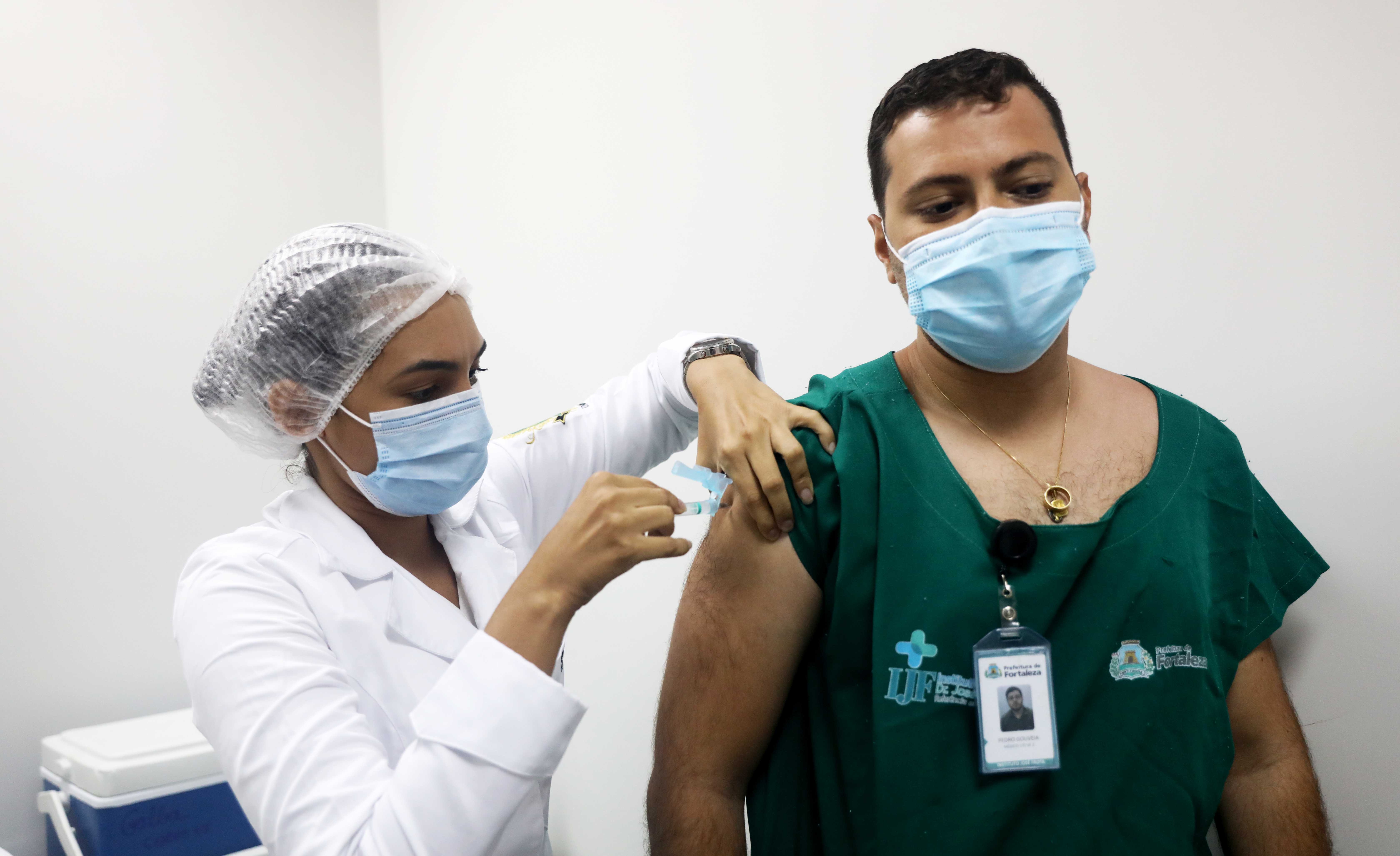 enfermeira usando máscara e touca aplicando vacina em homem funcionário do IJF, usando máscara, bata e crachá da Prefeitura